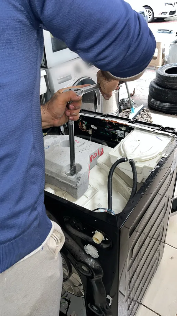Teknisyen çamaşır makinesinin kazan ağırlığını lokma anahtarla söküyor